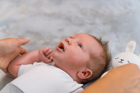 Development of a child. Closeup portrait of a dark-haired adorable newborn baby boy opening his mouth to communicate with his mother. Gray background. High quality photoの写真素材