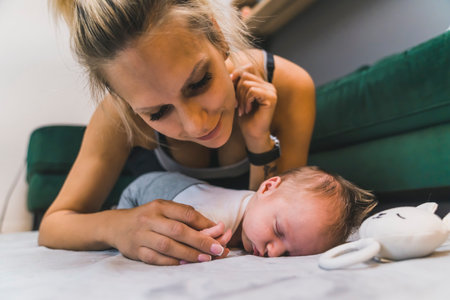 Floor perspective of a millennial caucasian skinny mother leaning over her adorable infant baby boy sleeping deeply next to his bunny rattle. Mother and son relationship. High quality photoの写真素材