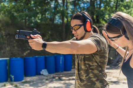male instructor showing a girl how to hold a pistol with a collimator and a torch correctly, medium...