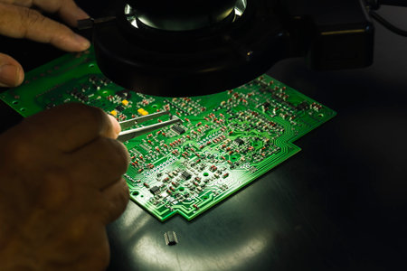 Professional repairman during work. Closeup shot of unrecognizable caucasian male engineer's hands during the use of specialistic tweezer to remove broken elements placed on printed circuit board. High quality photoの写真素材