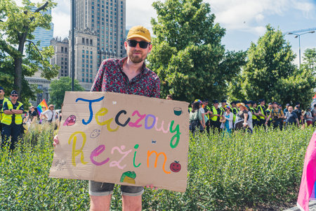 June 25, 2022 Warsaw, Poland - Warsaw Pride march in Poland on June 25, 2022. A man holding an LGBT placard with a message - Rainbow Regime. High quality photoのeditorial素材