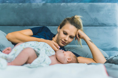 Caucasian beautiful young mom laying in bed with her newborn son wrapped in a baby blanket, talking to him, enjoying precious time with her child. High quality photoの写真素材