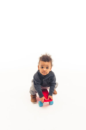 A little five years old afro-american guy sitting on a skateboard and looking into the camera - white background. High quality photoの写真素材