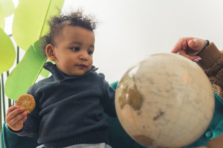 Small african american cutie boy is close to his mother who is pointing at the Globe - isolated. High quality photoの写真素材