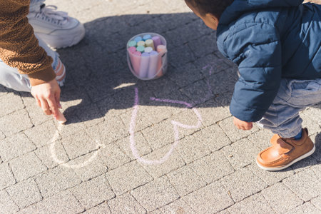 A small african 5 years old boy and his mother drawing hears on the pavement using colourful crayons. High quality photoの写真素材