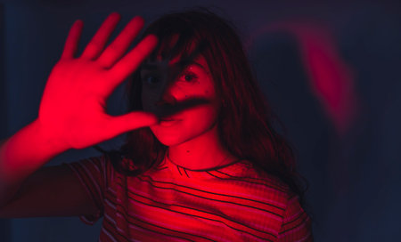 Artistic red lighting blocked by the hand of caucasian female posing model creating a shadow on her face. Stripped t-shirt. Modern viral aesthetic. High quality photoの写真素材