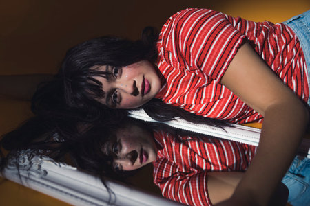 Conceptual mirror studio shot. Young attractive caucasian black-haired young adult dressed in vivid...
