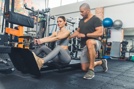 Young, athletic, caucasian woman performing seated back pull on the machine and her man coach...