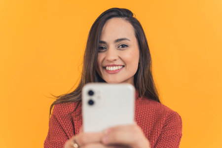 Front view of latin american woman with dark long hair smiling taking selfie with smartphone....