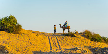 10.10.2022 Side, Turkey - Sandy hill with tourist photographing people riding camel in bright morning summer sunlight. Tourist destination. Horizontal outdoor shot. High quality photoのeditorial素材
