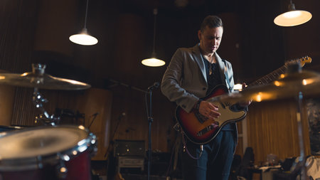 Man playing electric guitar in a studio around musical instruments and equipment. High quality photo