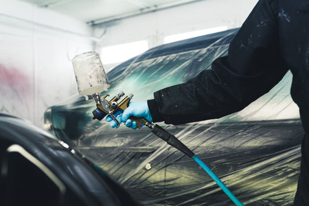 Use of paint spray gun. Indoor shot of an arm of a person in protective coveralls and gloves holding paint spray gun in a paint spray booth. High quality photoの写真素材
