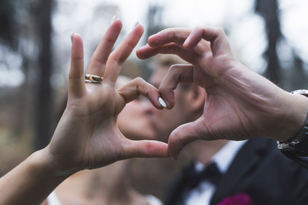 Symbolic heart sign done by just married heterosexual couple. Outdoor just married photoshoot. Blurred kissing Turkish wife and Scandinavian husband. High quality photoの写真素材