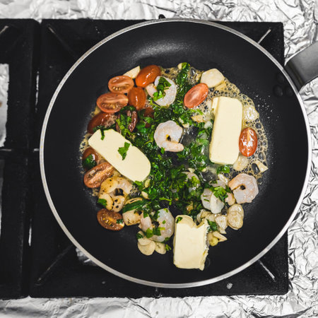 Shrimps, cherry tomatoes, parsley, and butter on frying pan. Cooking process and dish preparation. High angle view. High quality photoの写真素材