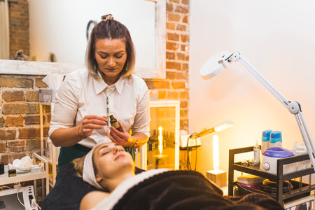 Front view of beautician putting an oil on her happy blonde clients face. . High quality photoの写真素材