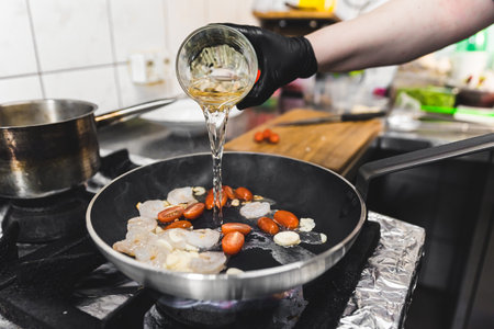 Chef adding white wine to the frying pan. Shrimps cooked with cherry tomatoes in white wine. Restaurant kitchen interior. High quality photoの写真素材