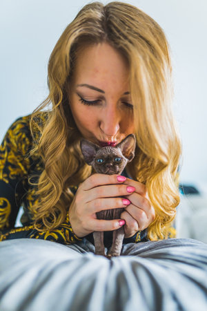 A blonde woman kissing the top of a Devon rex cat head. Pet concept. Vertical. . High quality photo