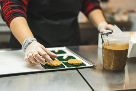 Baker placing cookies on green square plates on a baking tray. Carmel icing in a plastic cup placed...