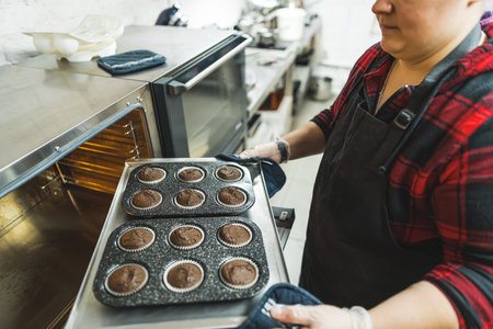 Pastry chef taking out trays with chocolate muffins out of an oven. Preparation of pastry and sweets. High quality photoの写真素材