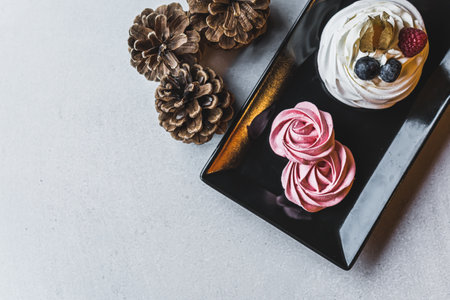 Little pavlova meringue cake with cream and berry on black plate standing next to cones on gray table. High angle. Copy space. High quality photoの写真素材