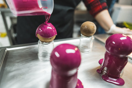 Round cakes put on small glass jars being decorated with pink glaze on a metal baking tray. Blurred background. . High quality photoの写真素材
