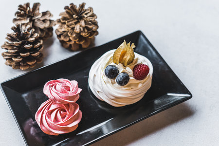 High angle shot of small meringue dessert with berries on black plate standing next to cones. Gray...
