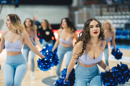 Attractive cheerleaders are dancing with energy and enthusiasm in revealing outfits. Theyre holding bright blue pom-poms to support their team.の写真素材