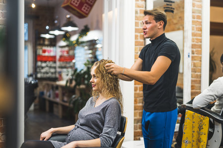handsome hairdresser man touching his clients wet hair before drying, medium-full shot. High quality photoの写真素材