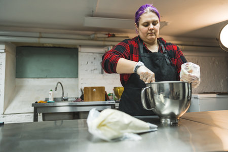 medium shot of a female baker working in the kitchen and glazing in an icing bag in front of her on the table. High quality photoの写真素材