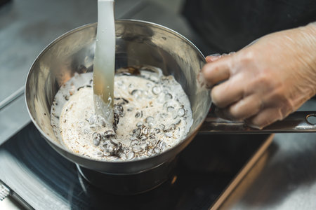 Close-up shot of unrecognisable baker melting chocolate with cream in water bath to prepare chocolate ganache. Professional baking process. Horizontal indoor shot. High quality photoの写真素材