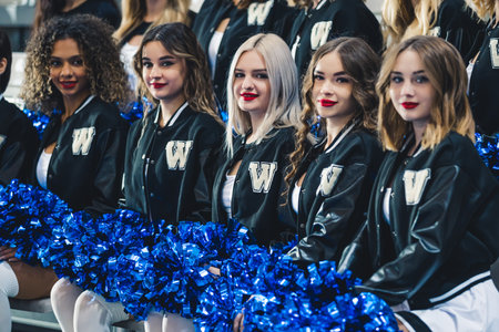Five cheerleaders sitting down holding blue pom-poms and looking at the camera. Sport concept. High...