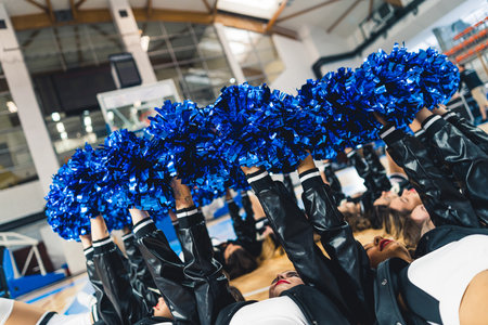 Side view of cheerleaders laying on basketball court and holding their blue pom-poms up in a circle. High quality photoの写真素材