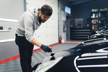 Male mechanic using car detailing brush kit on his clients black sports car. Professional maintenance of a car. Workshop interior. High quality photoの写真素材