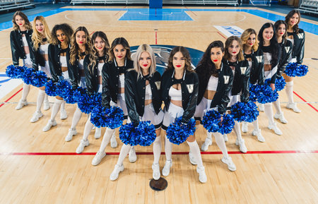 Top view of female cheerleaders standing in v formation on basketball court with blue pom-poms in their hands. High quality photoの写真素材