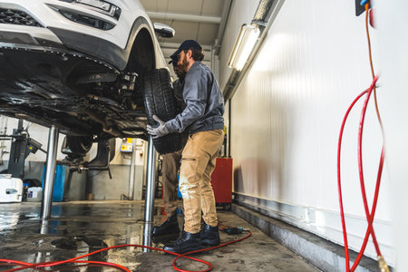 Car mechanics are busy replacing the wheels of a car on the lift in an auto repair shop....