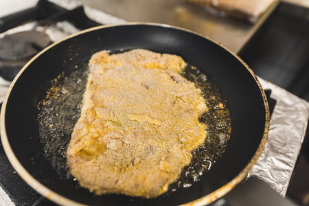 Frying breaded pork cutlet schabowy in oil in a frying pan. Restaurant kitchen food preparation process. Horizontal indoor shot. High quality photoの写真素材