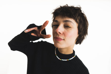 Cool short-haired Gen Z woman blinking at camera and showing v sign. Modern teenagers and people in...