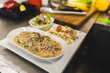 Plating pork fillet dish with bolet mushroom gravy sauce pork dumplings and salad. Restaurant kitchen food plating process. Horizontal indoor shot. High quality photoの写真素材
