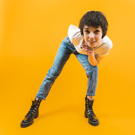 Portrait of young confident woman leaning towards and smiling at camera. Square full-length shot. Orange background. Copy space. High quality photoの写真素材
