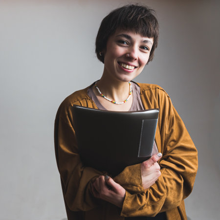 Medium shot of a smiling female model posing with a binder in her hands. Grey background. Vertical photo. High quality photoの写真素材