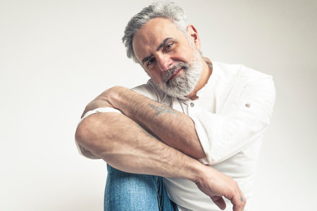Gray haired bearded man wearing a white shirt and denim posing for camera - isolated over white background. High quality photoの写真素材