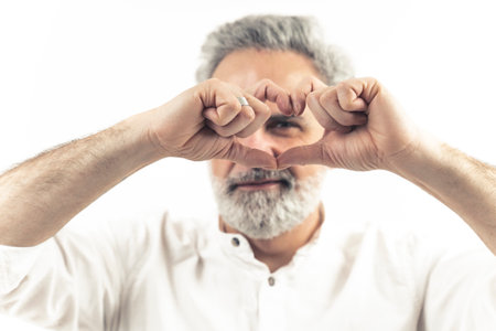 Middle-aged bearded man making heart shape with his hands close to his eyes - Isolated on white background. High quality photoの写真素材