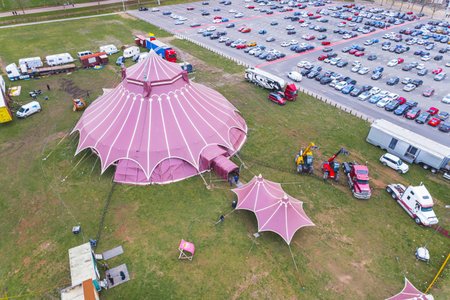 Red circus tent seen from aerial perspective standing on a grass field next to car parking lot....