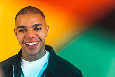 Bald positive Black man in his 20s smiling at camera. Studio portrait over yellow background. Red and green filter foils in the foreground. High quality photoの写真素材