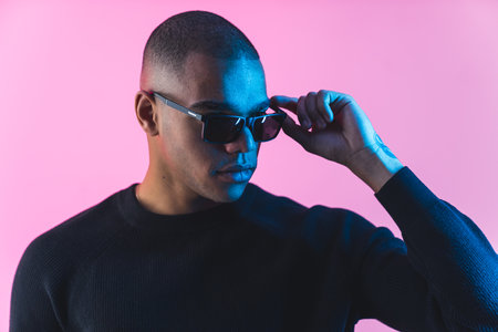 Eyewear concept. Elegant serious bald male model looking away and touching the frame of sunglasses....