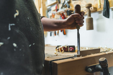 Chisel in use. Closeup shot of professional male carpenter holding one of his chisels to shape, carve and cut wood. High quality photoの写真素材