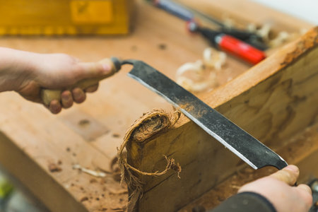 Shaping wood concept. Professional woodworker using drawshave with both hands to shape piece of wood. Closeup shot. High quality photoの写真素材