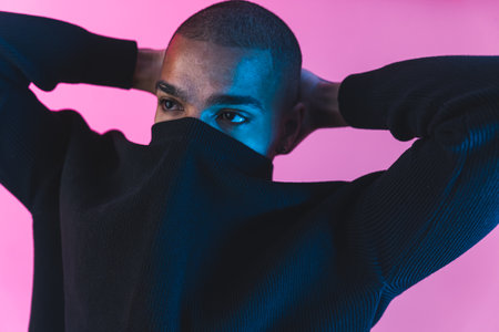 Unrecognisable incognito male model with face covered by his black hoodie over pink background. Face covering concept. High quality photoの写真素材