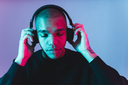 Afro-American young man with headphones listening to the music and relaxing, blue background. High quality photoの写真素材