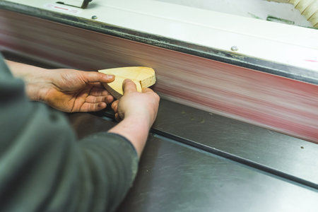 Male carpenter holding wooden heart and using grinding machine. Machine with sand paper used in workshop. High quality photoの写真素材